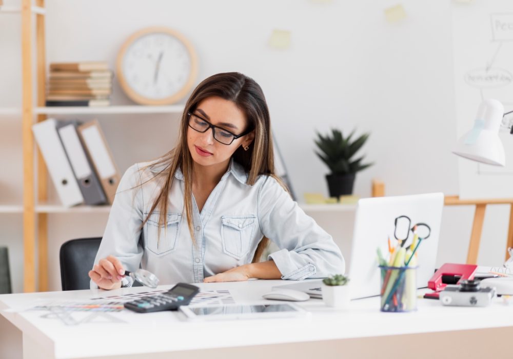 beautiful-woman-sitting-office-holding-magnifying-glass